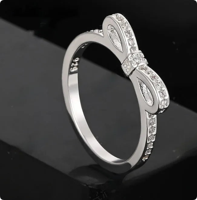 Silver bow-shaped ring with zircon crystals on a finger, showing detailed bow motif design