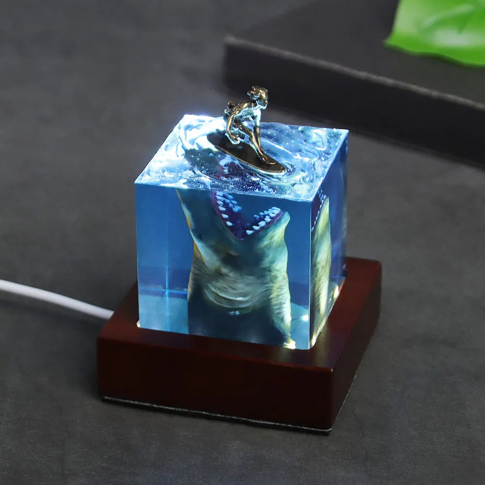 Clear epoxy resin ornament with a detailed shark surfing scene inside, shown next to its integrated lamp holder.