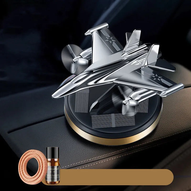 Silver solar powered rotating fighter plane air freshener ornament on a car dashboard.