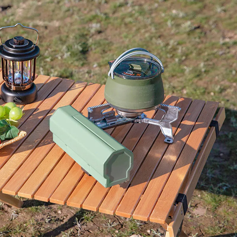Green portable folding gas stove with serrated pot support and adjustable valve, shown with storage bag.