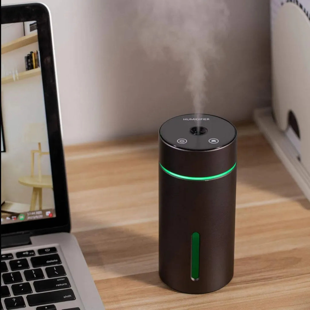 Black aluminium car humidifier and essential oil diffuser with night light on a desk next to USB cable.
