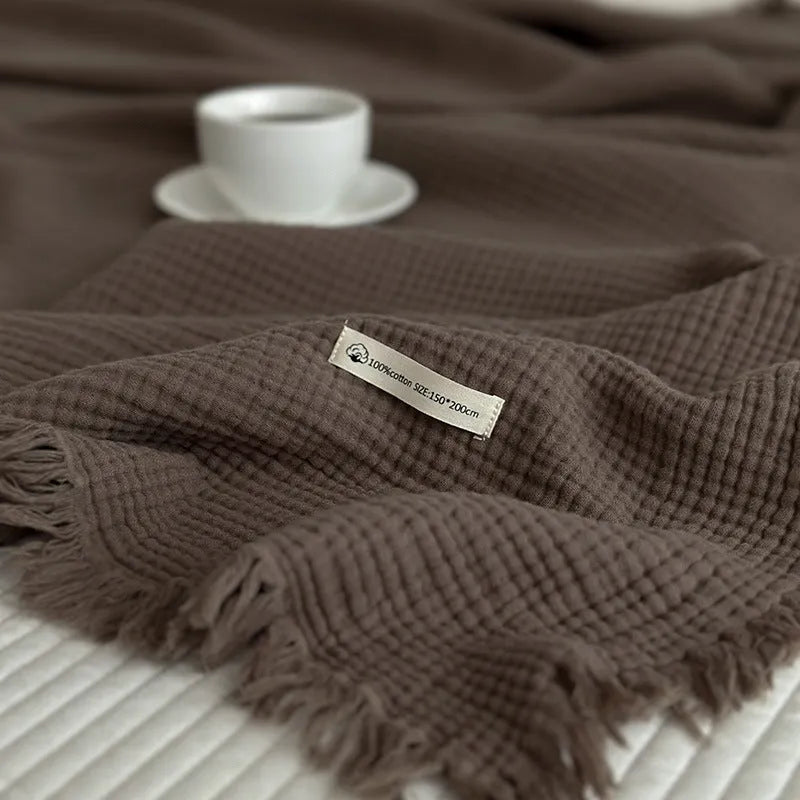 Four-layer cotton gauze blanket with tassel trim in avocado green colour laid flat.
