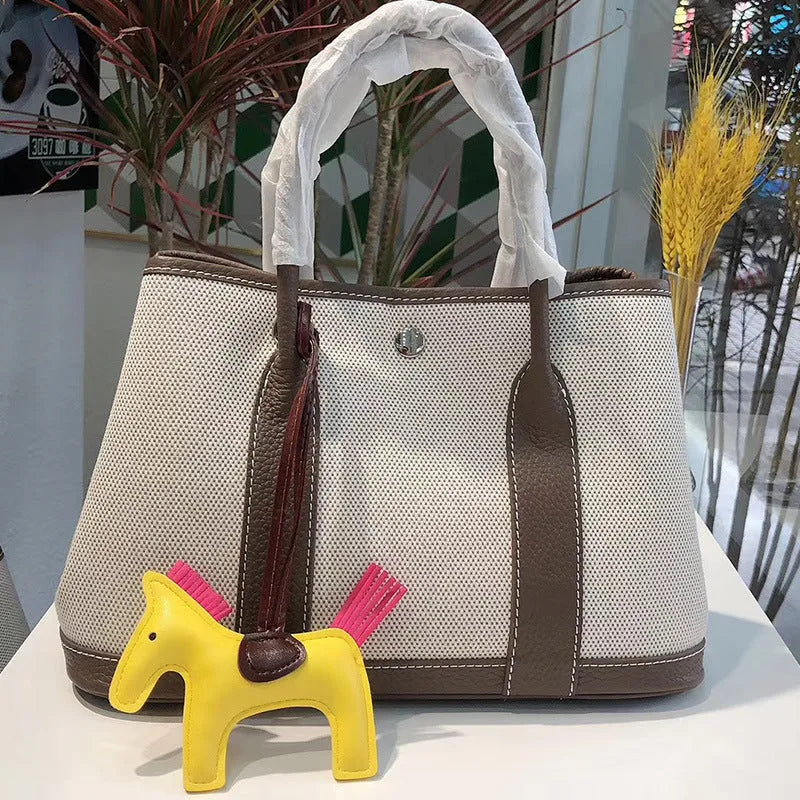 Women's canvas tote bag with genuine leather trim in bucket shape showing internal zip compartments