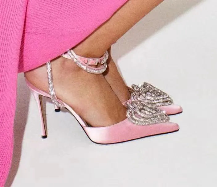 Women's black satin sandals with a heart-shaped rhinestone and pointed toe, showing the adjustable cross-strap fastening.