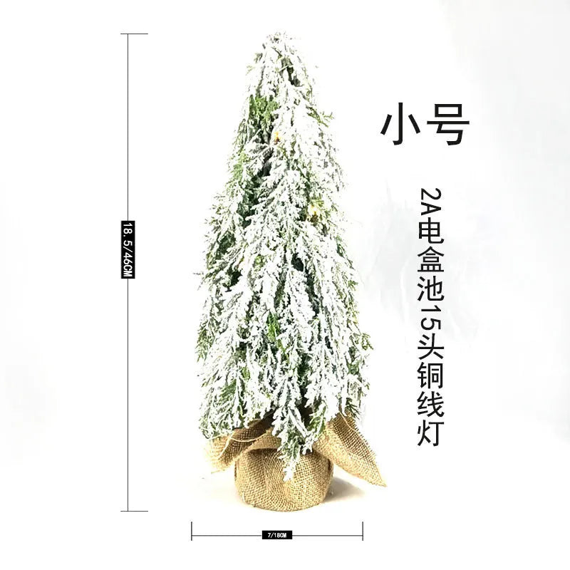 Small 24-inch artificial Christmas tree with snow sprayer finish and integrated lights on desktop