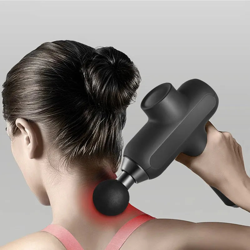 Handheld black electric muscle massager with six different massage heads on a table.