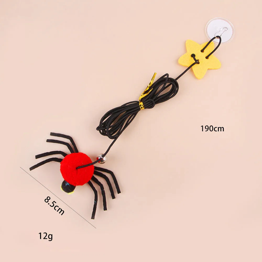 Red hanging cat toy with feather wand, bells, and spider on elastic rope, mounted on a door.