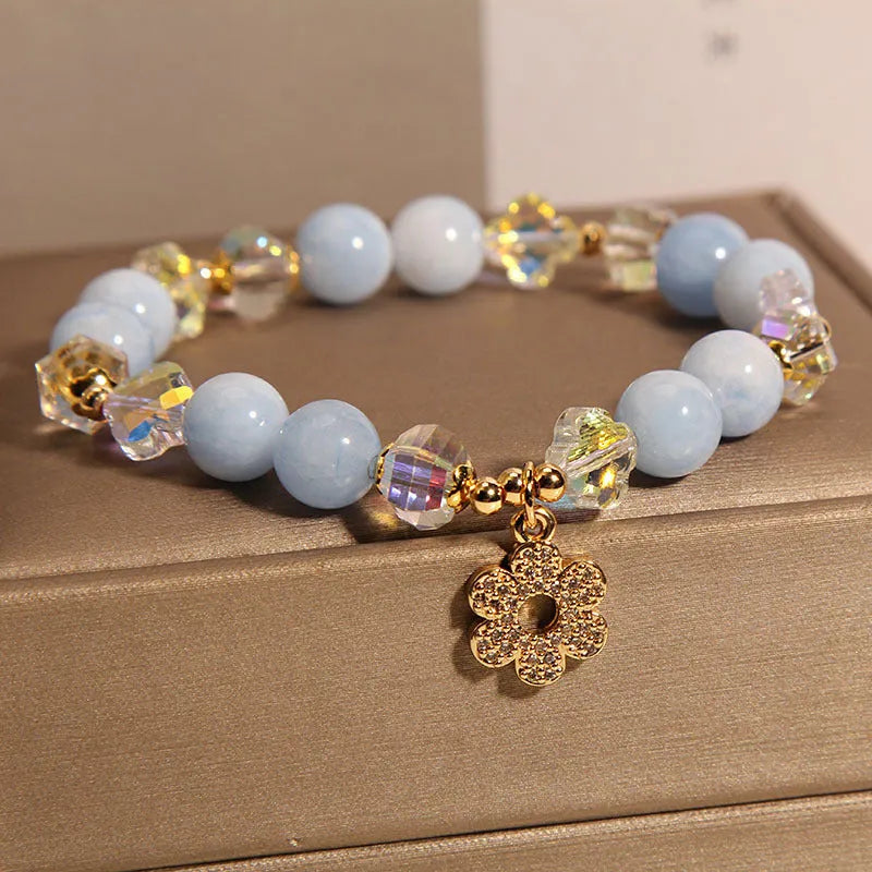 Women's aquamarine crystal bracelet with a four-leaf clover charm and pearl details on a white background