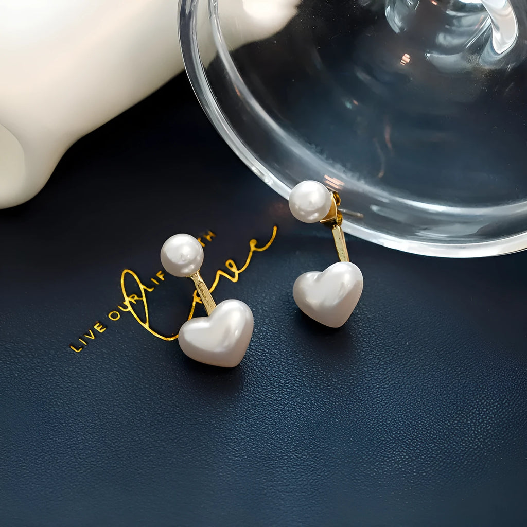 Close-up of women's silver-toned heart-shaped stud earrings with a central inlaid artificial pearl or gemstone.