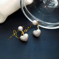 Close-up of women's silver-toned heart-shaped stud earrings with a central inlaid artificial pearl or gemstone.