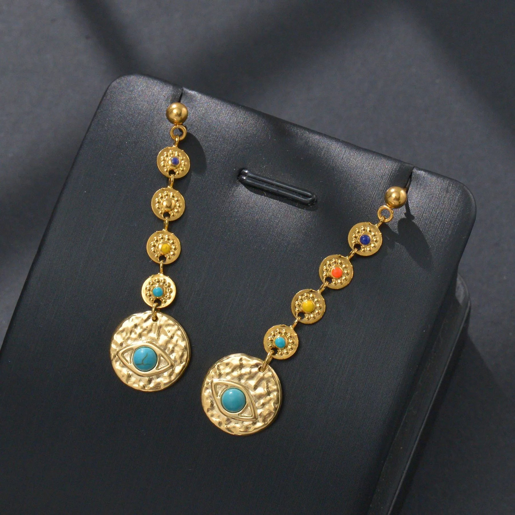 A pair of stainless steel geometric earrings showing star, eye, and shell sun designs.