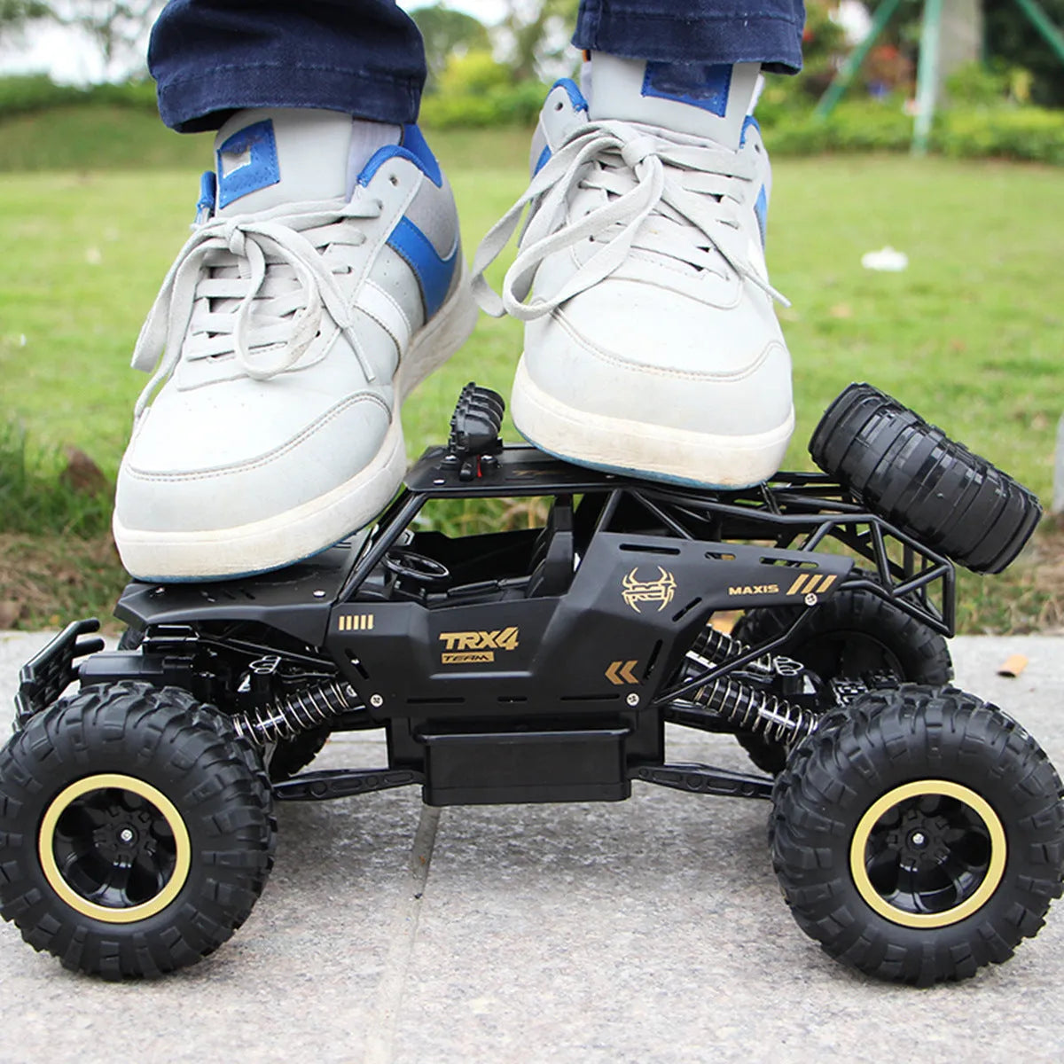 Large black and silver 4WD remote control off-road climbing cars with wireless controller on a rocky surface.