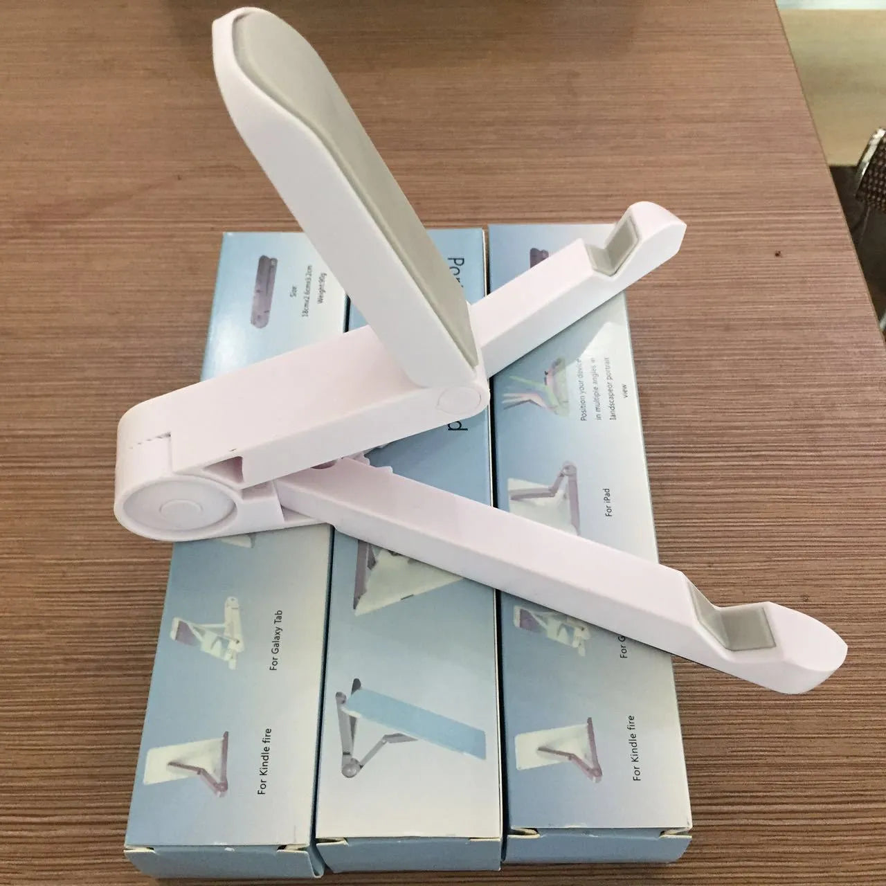 Black foldable aluminium tablet holder showing adjustable stand in open and closed positions on a desk.