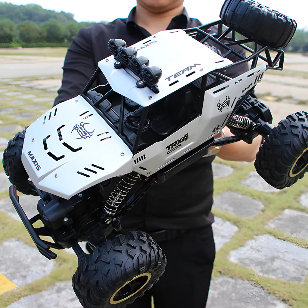 Large black and silver 4WD remote control off-road climbing cars with wireless controller on a rocky surface.
