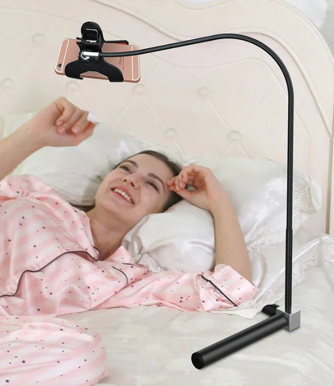 Black bedside mobile phone holder mounted on a bed frame with a phone securely clipped in place.