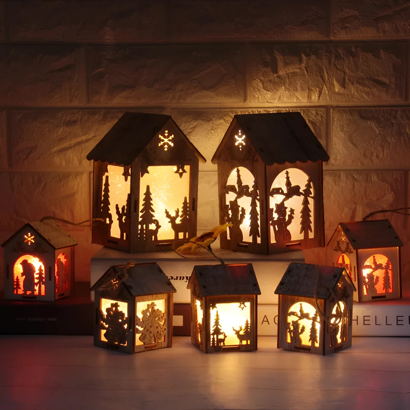 Three handcrafted wooden Christmas house decorations on a rustic table: a log bell, a painted old man cottage, and a snowman house.