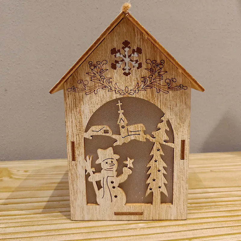 Three handcrafted wooden Christmas house decorations on a rustic table: a log bell, a painted old man cottage, and a snowman house.
