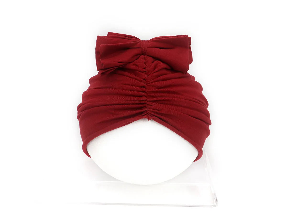 Soft acrylic knitted baby girl turban hat in a solid colour, shown on an infant.