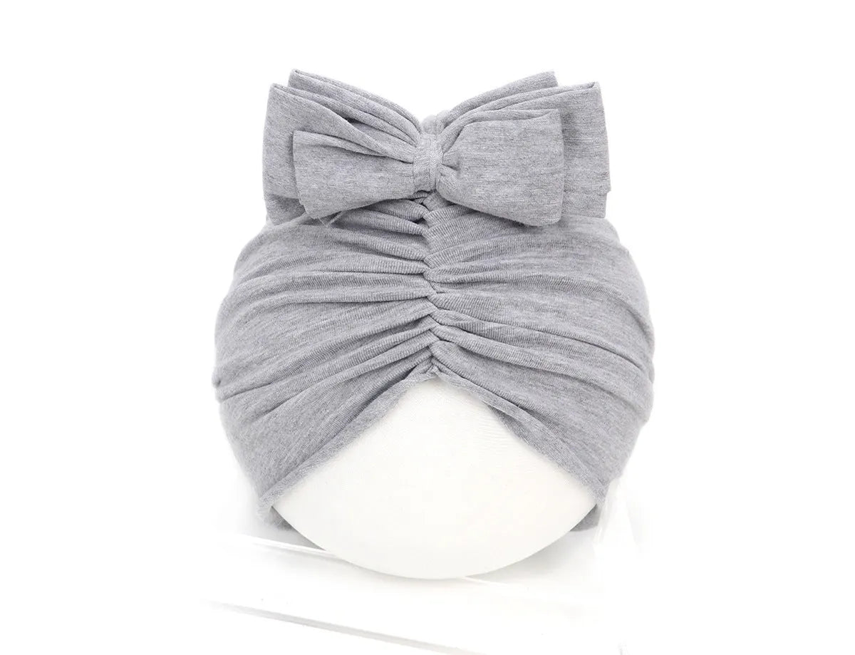 Soft acrylic knitted baby girl turban hat in a solid colour, shown on an infant.
