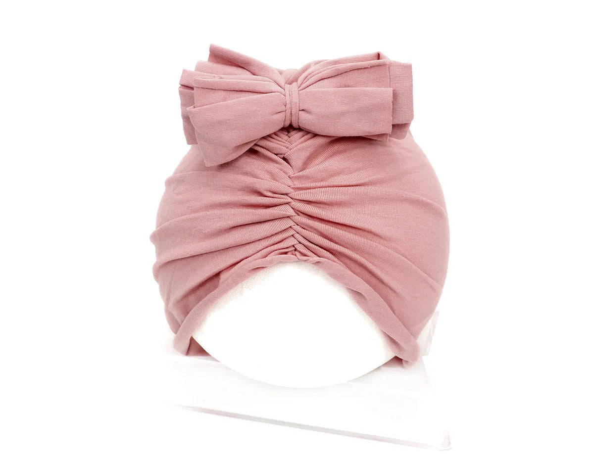 Soft acrylic knitted baby girl turban hat in a solid colour, shown on an infant.