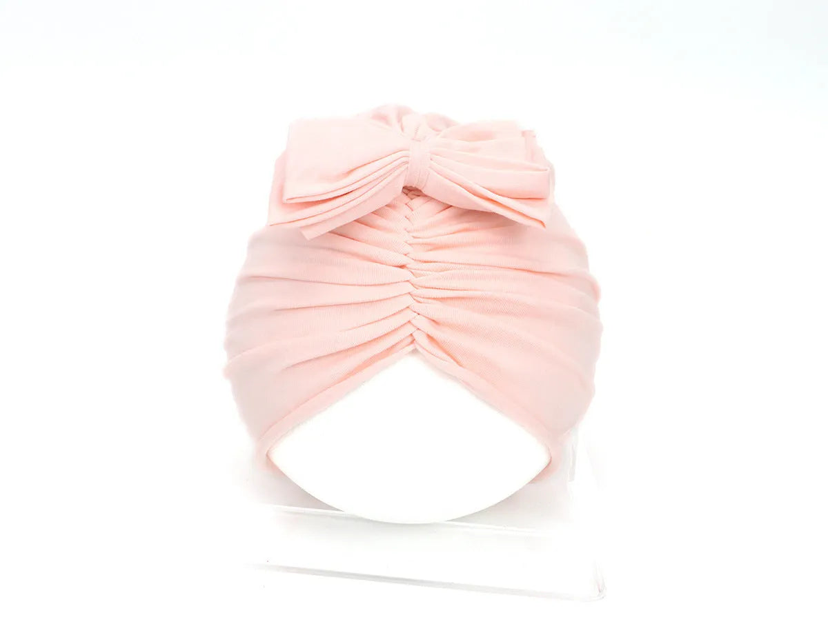 Soft acrylic knitted baby girl turban hat in a solid colour, shown on an infant.