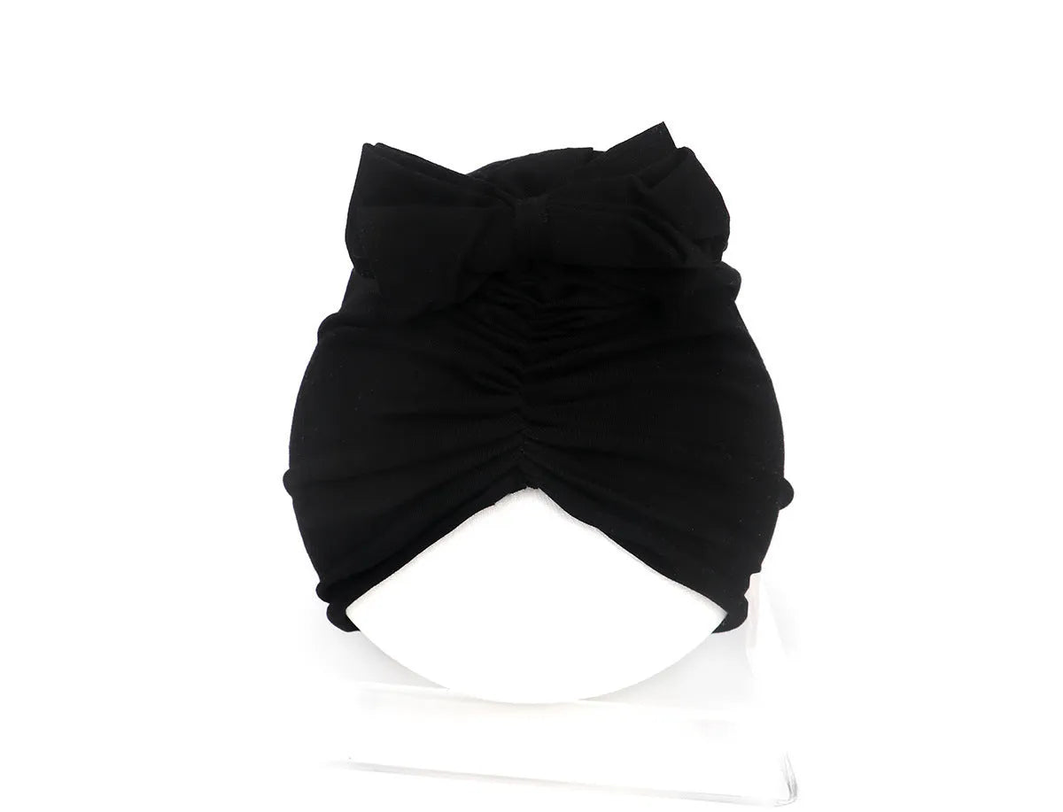 Soft acrylic knitted baby girl turban hat in a solid colour, shown on an infant.