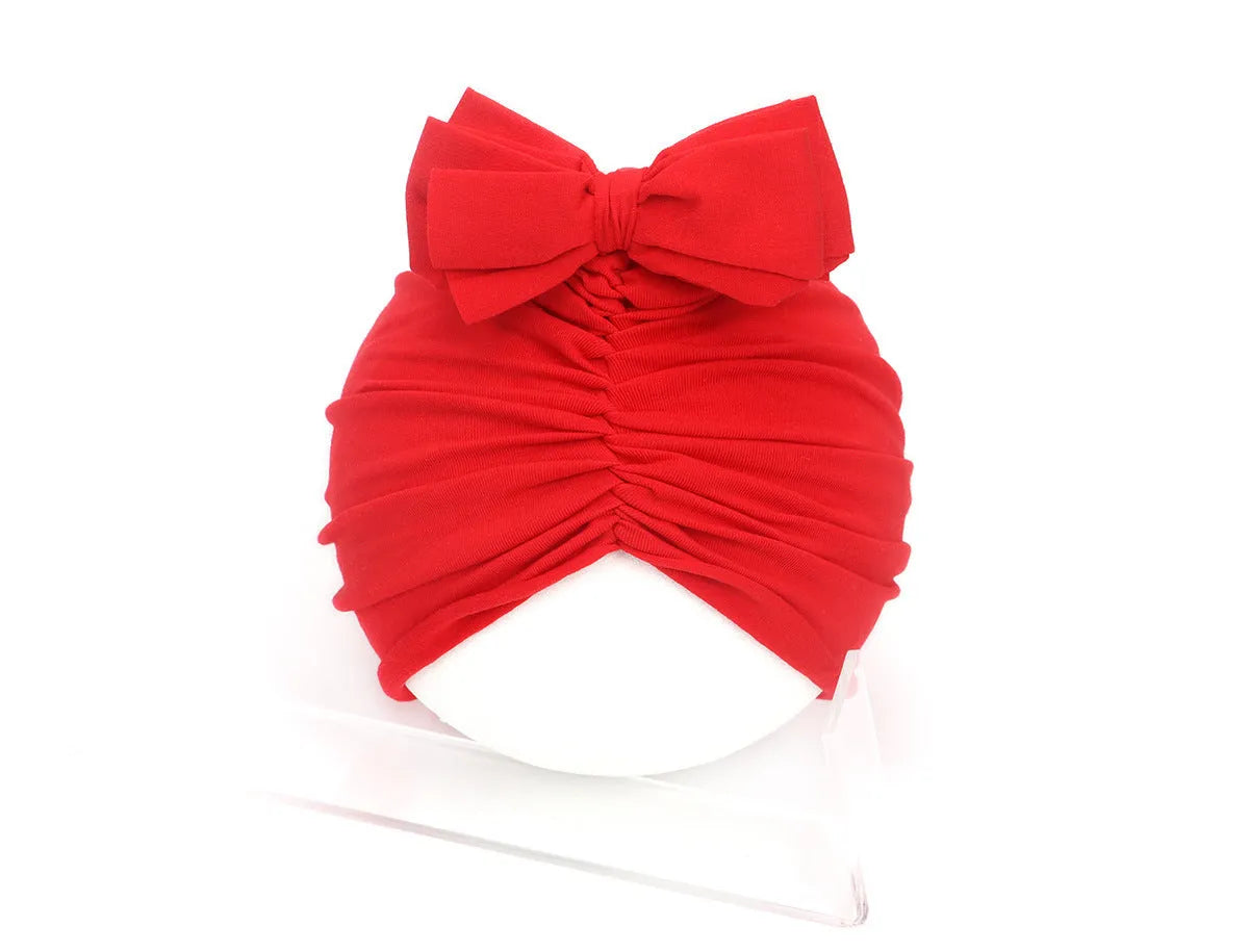 Soft acrylic knitted baby girl turban hat in a solid colour, shown on an infant.