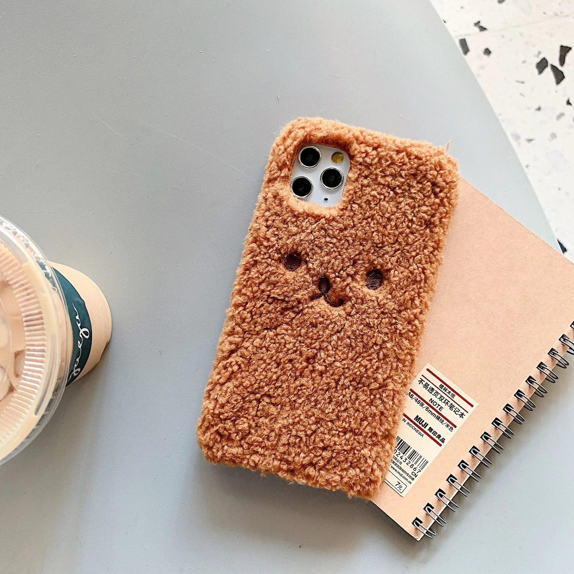 Brown TPU iPhone case with a soft embroidered plush cartoon bear face on the back.