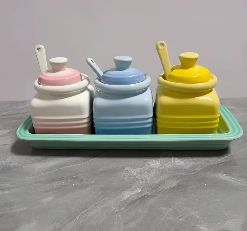 Ceramic seasoning jar set with three pots and spoons on a kitchen countertop