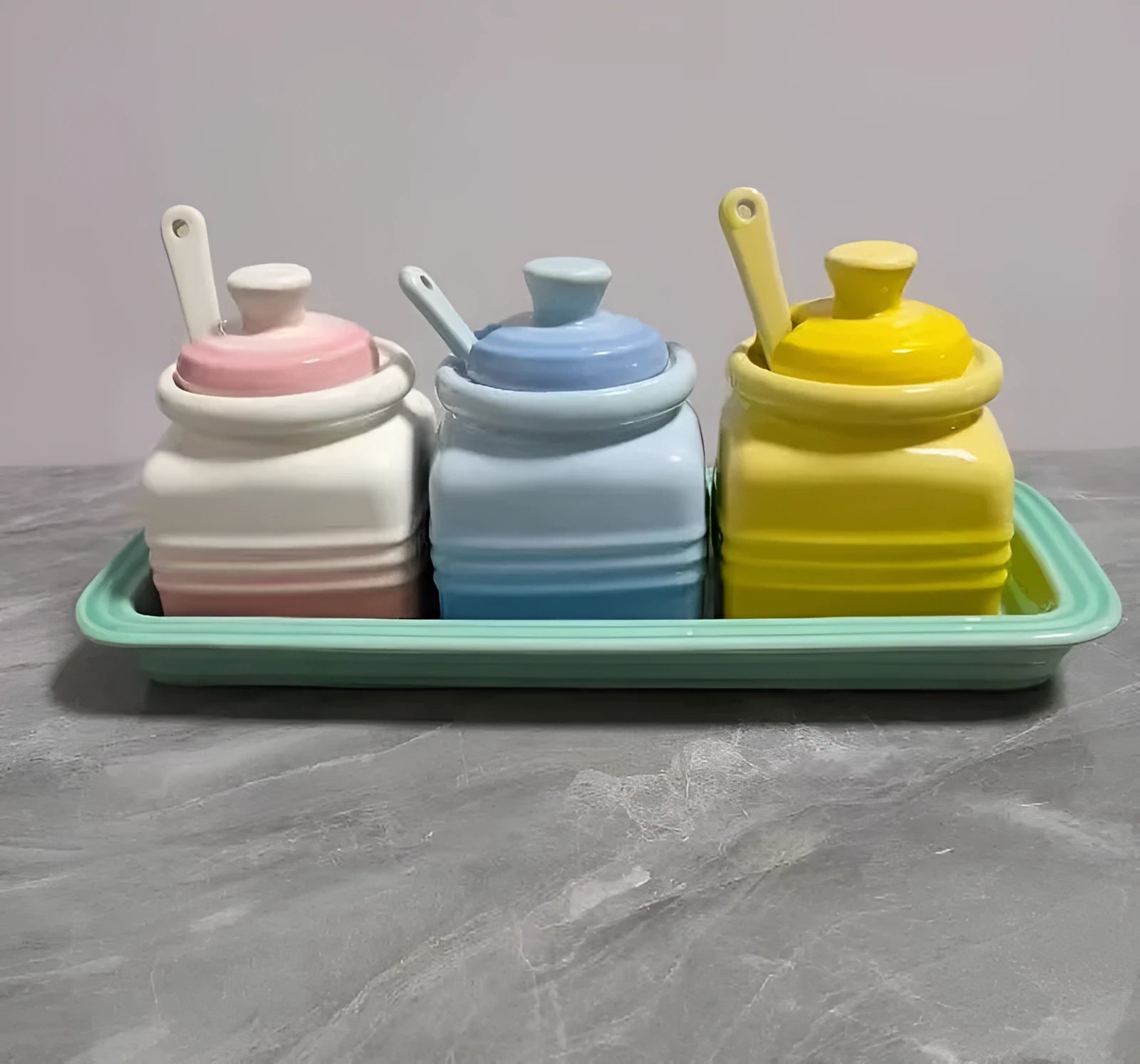 Ceramic seasoning jar set with three pots and spoons on a kitchen countertop