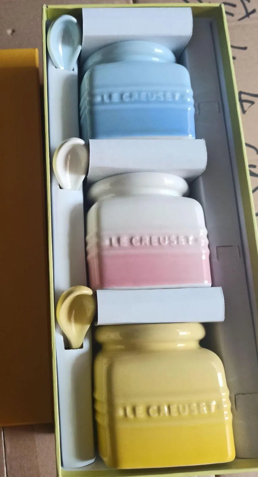 Ceramic seasoning jar set with three pots and spoons on a kitchen countertop