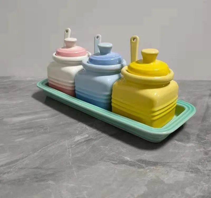 Ceramic seasoning jar set with three pots and spoons on a kitchen countertop