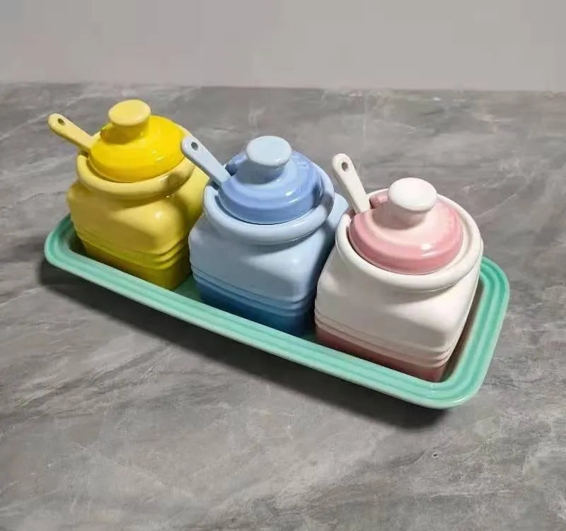 Ceramic seasoning jar set with three pots and spoons on a kitchen countertop