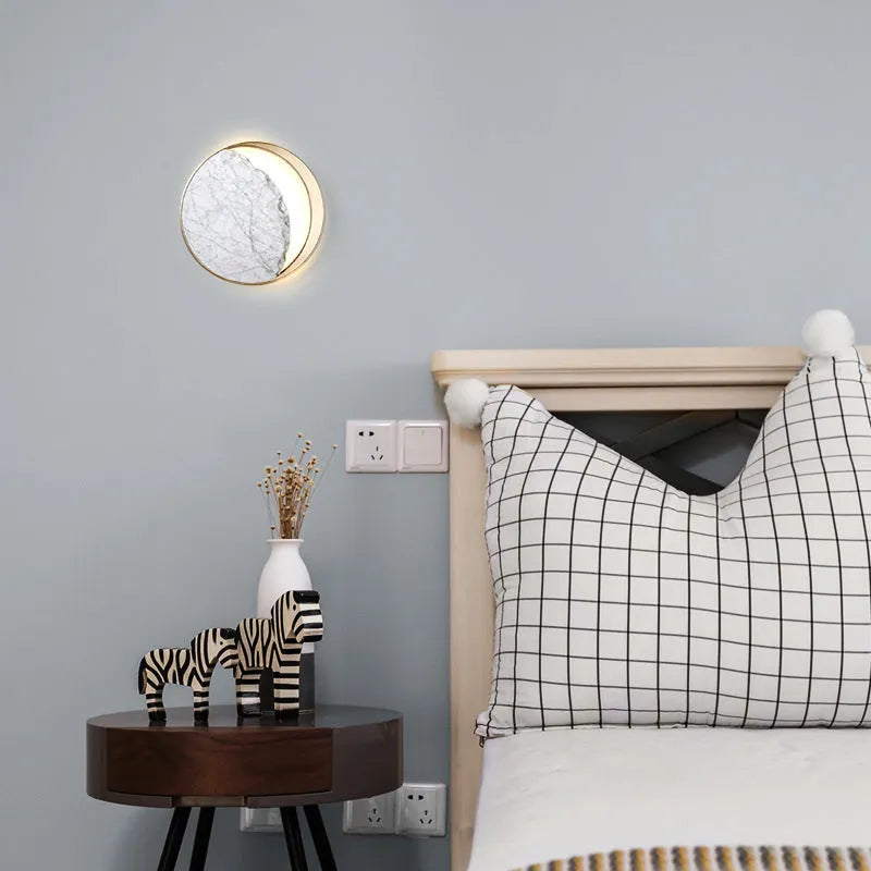 Round marble and copper LED wall lamp with eclipse design, 25 cm diameter, on a textured wall