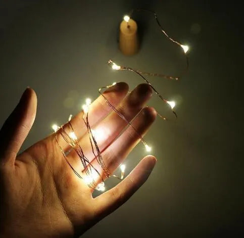 Copper wire LED string light with bottle stopper illuminated in a glass wine bottle.