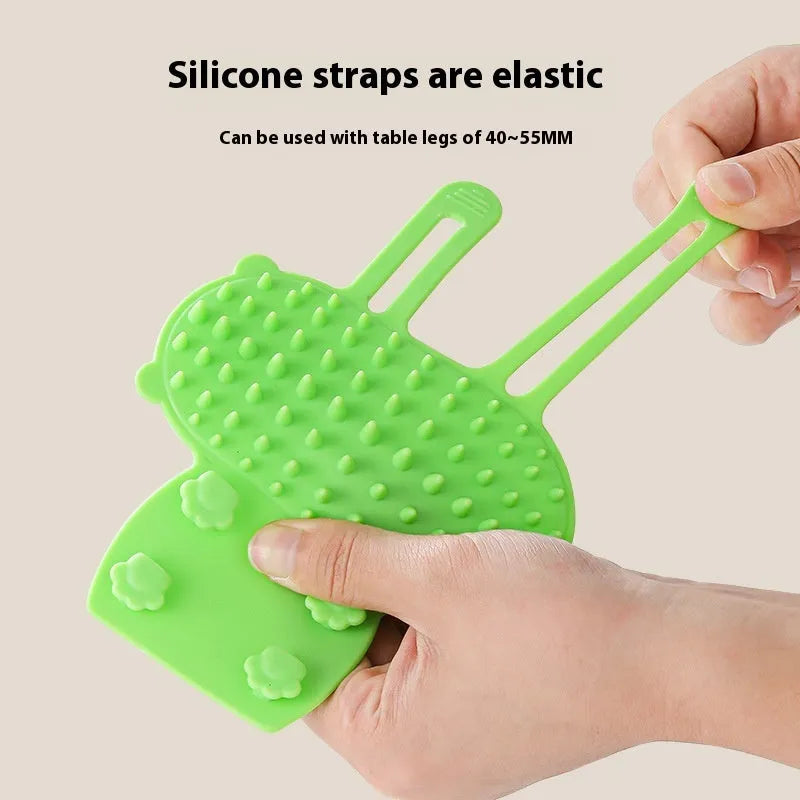 Silicone cat grooming and scratching brush with adjustable strap wrapped around a table leg.