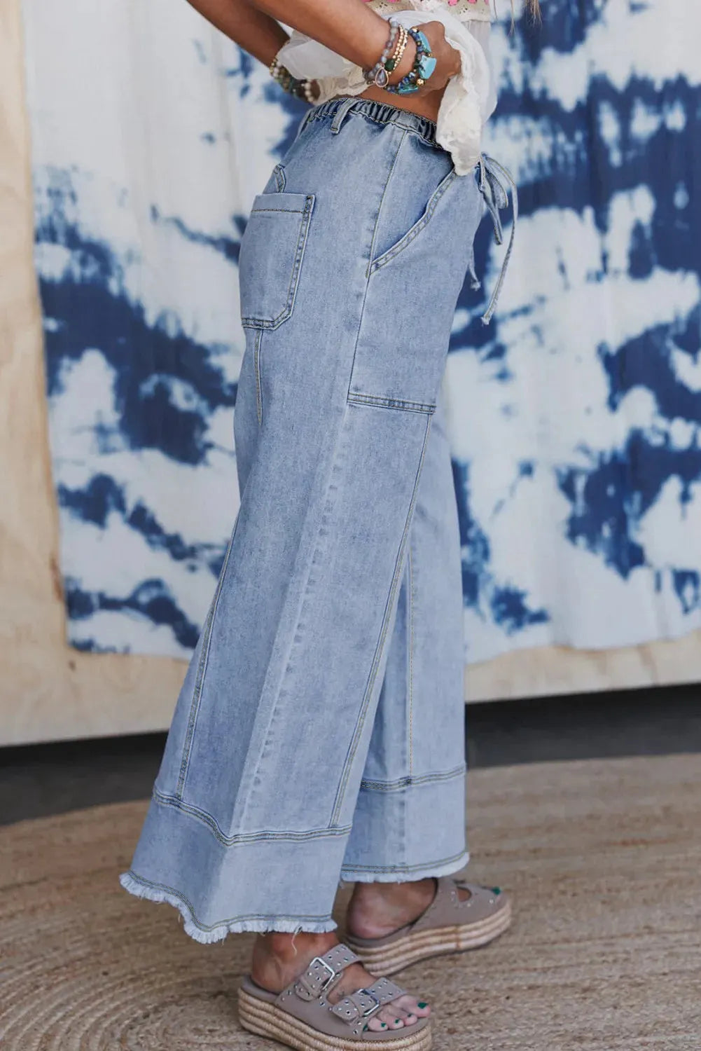 Beau blue wide leg denim pants on a hanger, showing drawstring waist and raw hem detail.