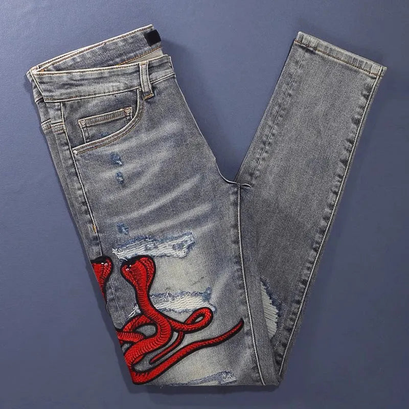 Slim fit blue jeans with distressed hole patches and embroidery on the legs, showing a washed-out colour.