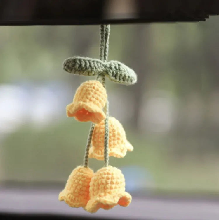 Green and white knitted wool car plant decoration hanging from a rope.