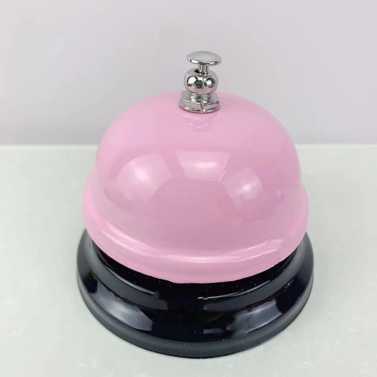 Iron call bell on a desk, shown in one of twelve available colours including red, blue, green, and pink.