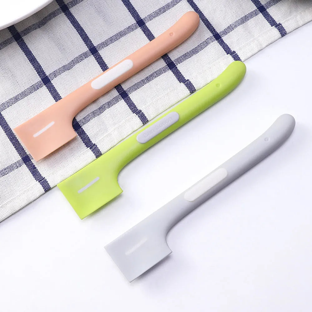 Long green handled pet food scoop next to a dog food tin, showing its right-angle scraping head.