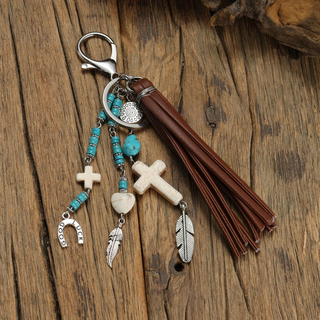 Alloy cross pendant keychain with leather rope and tassel in colour XY-3669 on a wooden surface