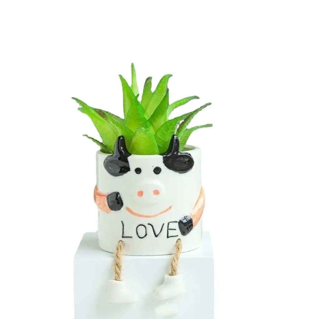 Small cartoon-style ceramic flowerpot with a raised hanging foot, on a desk next to a succulent.