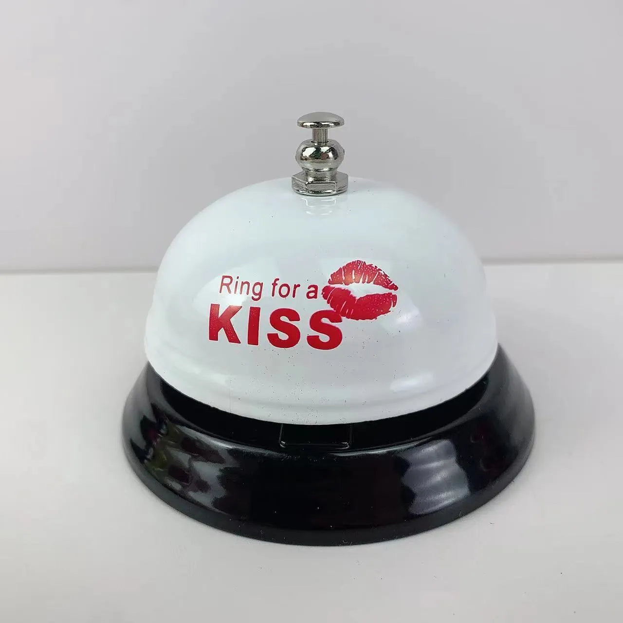 Iron call bell on a desk, shown in one of twelve available colours including red, blue, green, and pink.