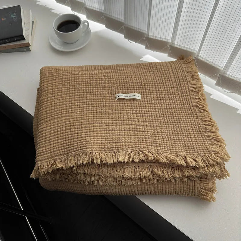 Four-layer cotton gauze blanket with tassel trim in avocado green colour laid flat.