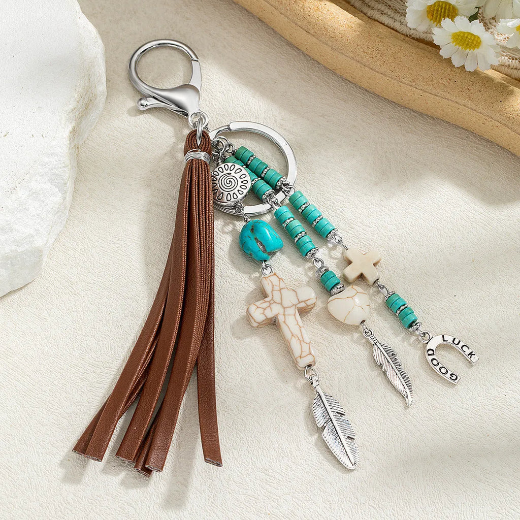 Alloy cross pendant keychain with leather rope and tassel in colour XY-3669 on a wooden surface
