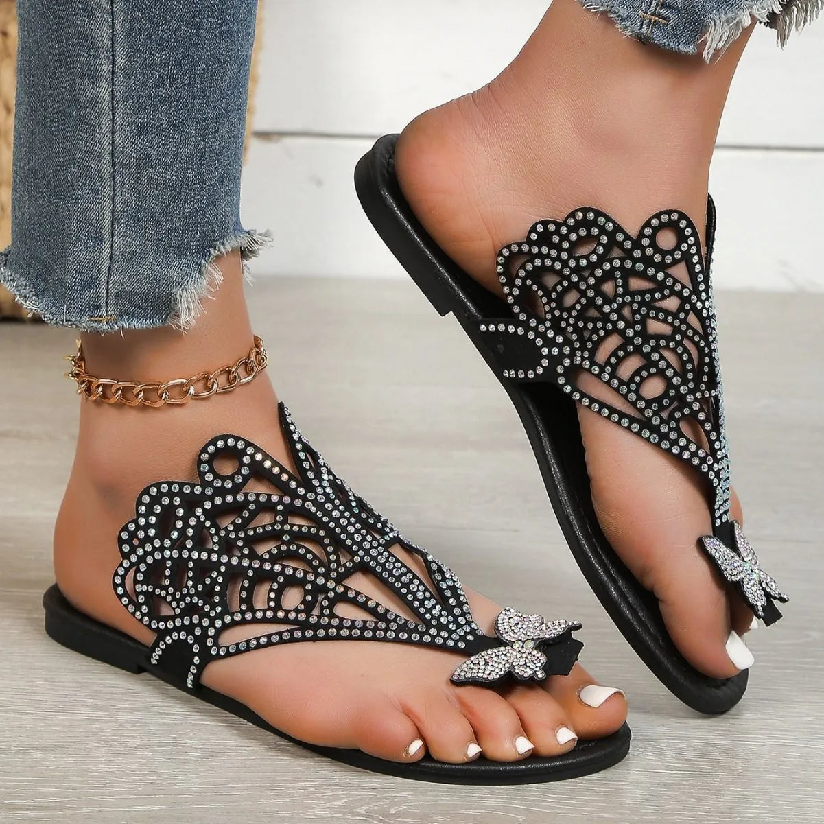 Women's black slip-on sandals with rhinestone accents and flip-toe design showing rubber sole
