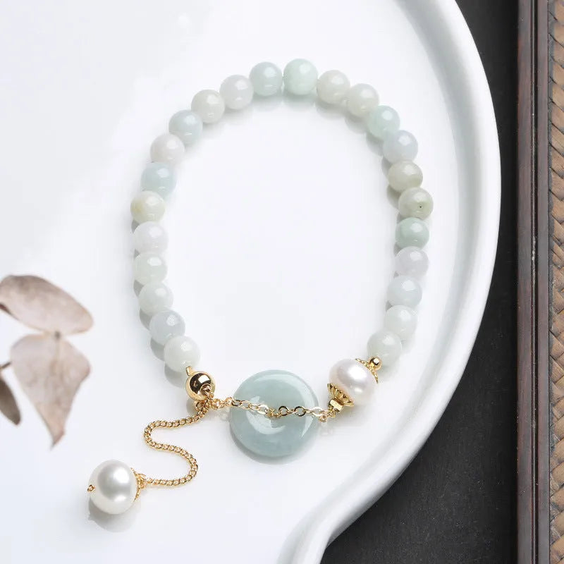 Close-up of a green jade and pearl bracelet with a geometric peace buckle on an elastic band.