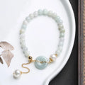 Close-up of a green jade and pearl bracelet with a geometric peace buckle on an elastic band.