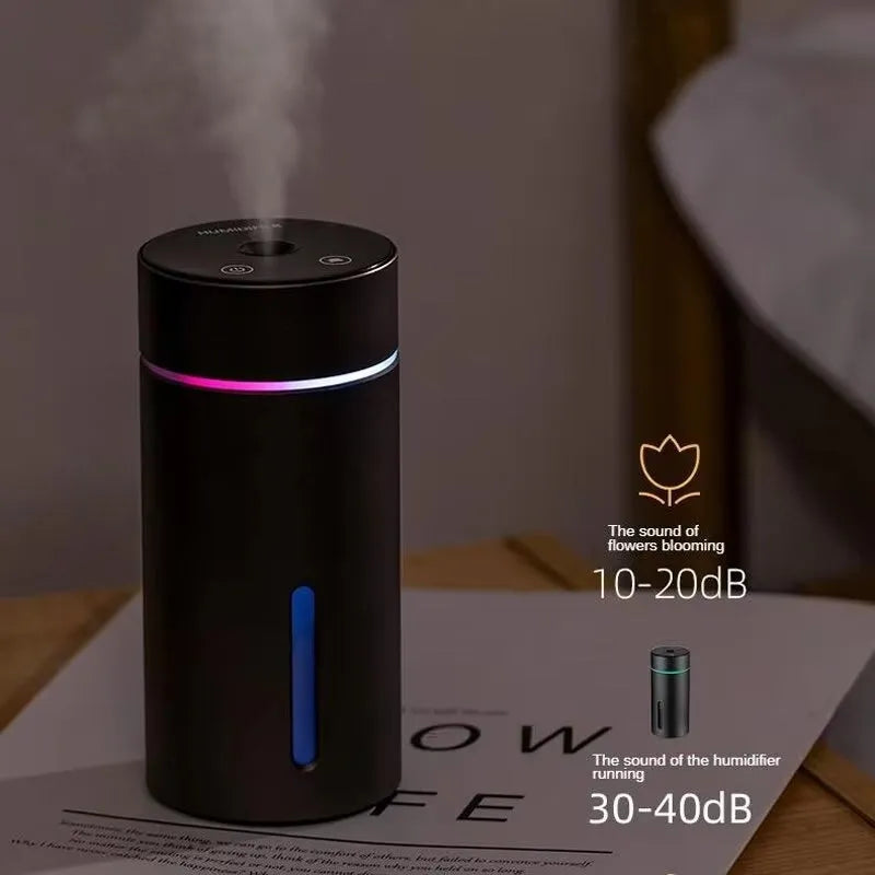 Black aluminium car humidifier and essential oil diffuser with night light on a desk next to USB cable.